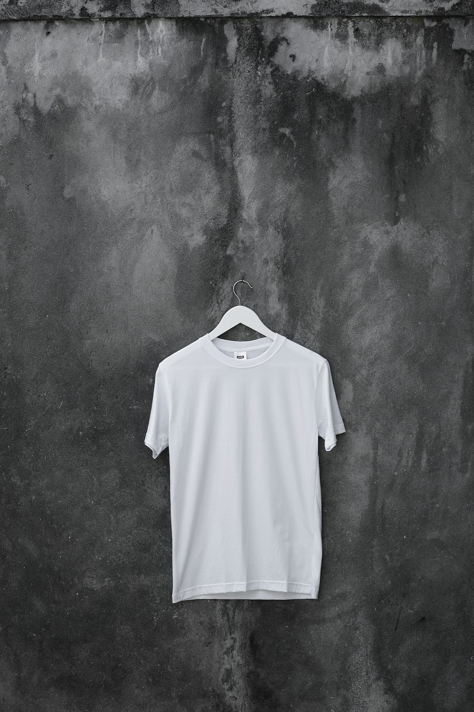 A white tee shirt on a hanger against a concrete wall